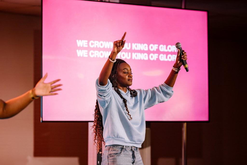 a girl stands on stage with both hands raised towards the sky, one hand is holding a microphone